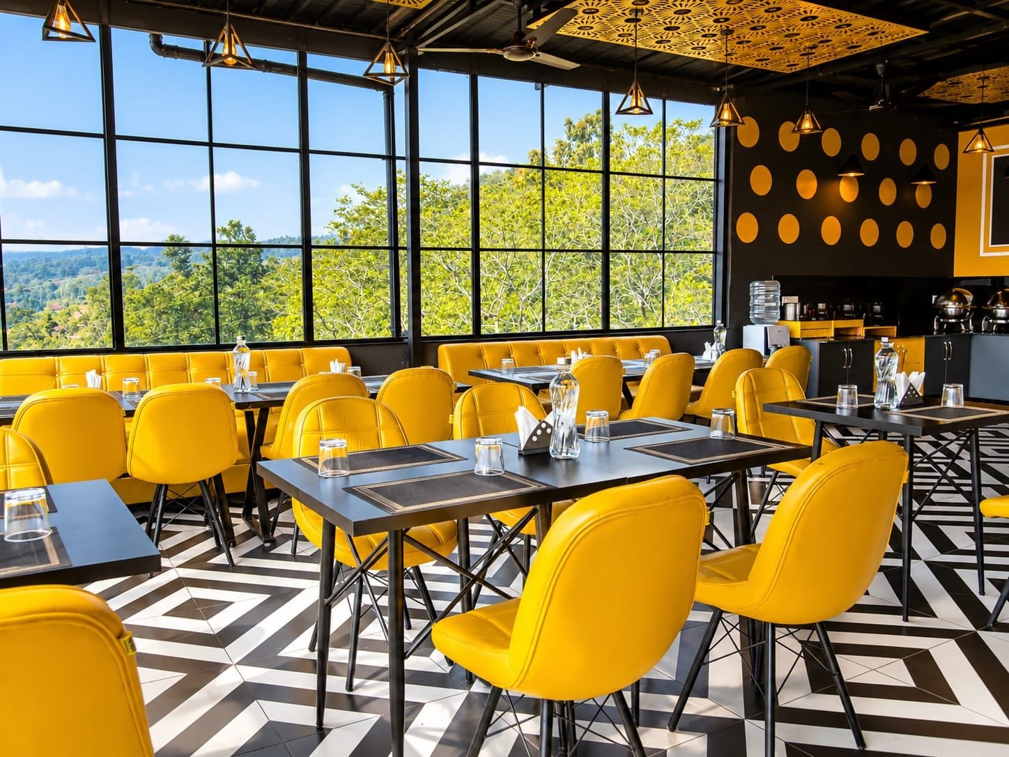 Un restaurante con sillas y mesas amarillas, ventanas amplias con vistas y un suelo estampado.