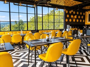 A restaurant with yellow chairs and tables, large windows with a view, and a patterned floor. - Hotel Celestial Ganges (Rishikesh)