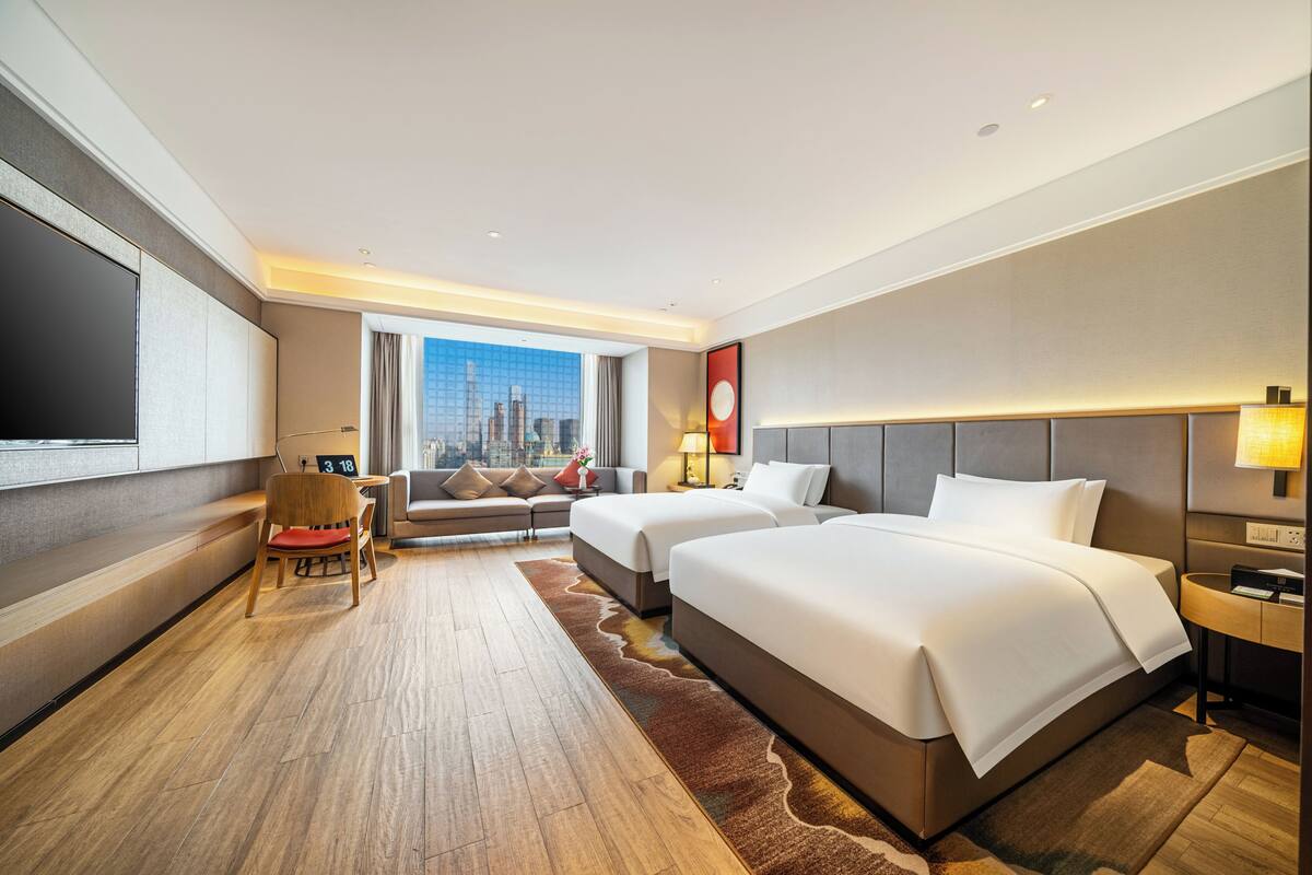 Habitación de hotel con dos camas, un sofá, un escritorio, una silla y un ventanal con vista a la ciudad.