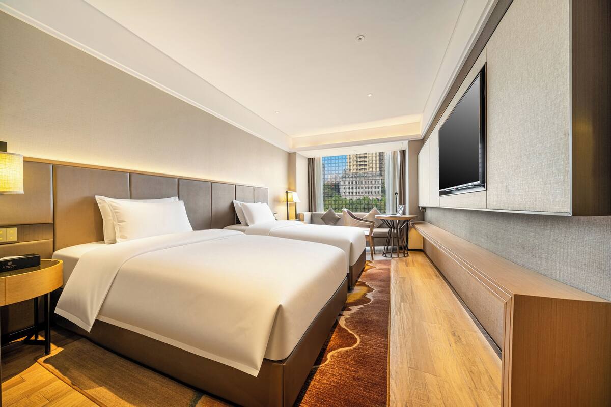 Habitación de hotel con dos camas, televisión, escritorio y vista a la ciudad.