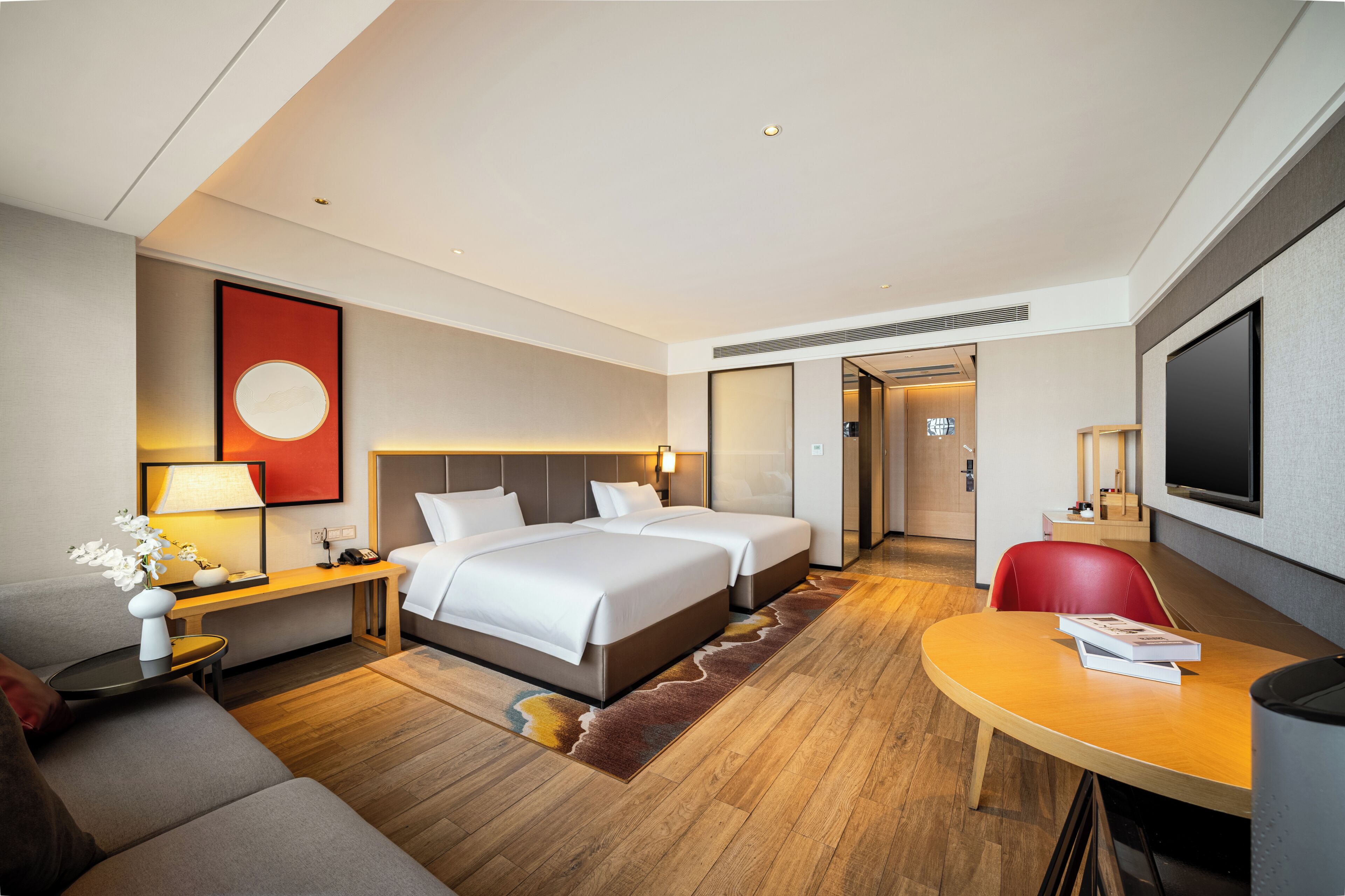 A hotel room with a bed, a desk, a chair, a TV, and a sofa.
