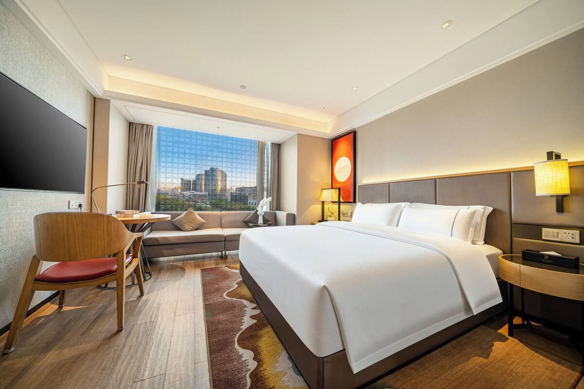 Habitación de hotel con una cama grande, un escritorio, una silla, un sofá y vistas a la ciudad.