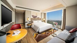 Habitación de hotel con cama, escritorio, silla, sofá, televisor y ventana con vista a la ciudad.