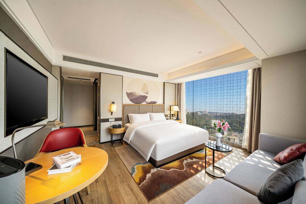 Habitación de hotel con cama, escritorio, silla, sofá, televisor y ventana con vista a la ciudad.
