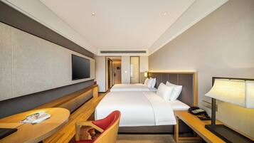 A hotel room with a large bed, a desk with a chair, a TV, and a bedside table with a lamp.