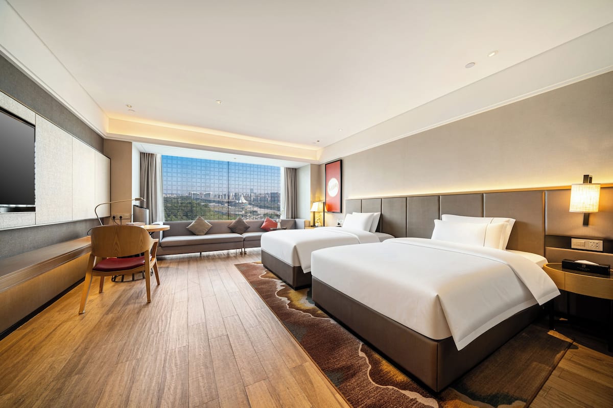 Habitación de hotel con dos camas, un sofá, una silla, un televisor y vista a la ciudad.