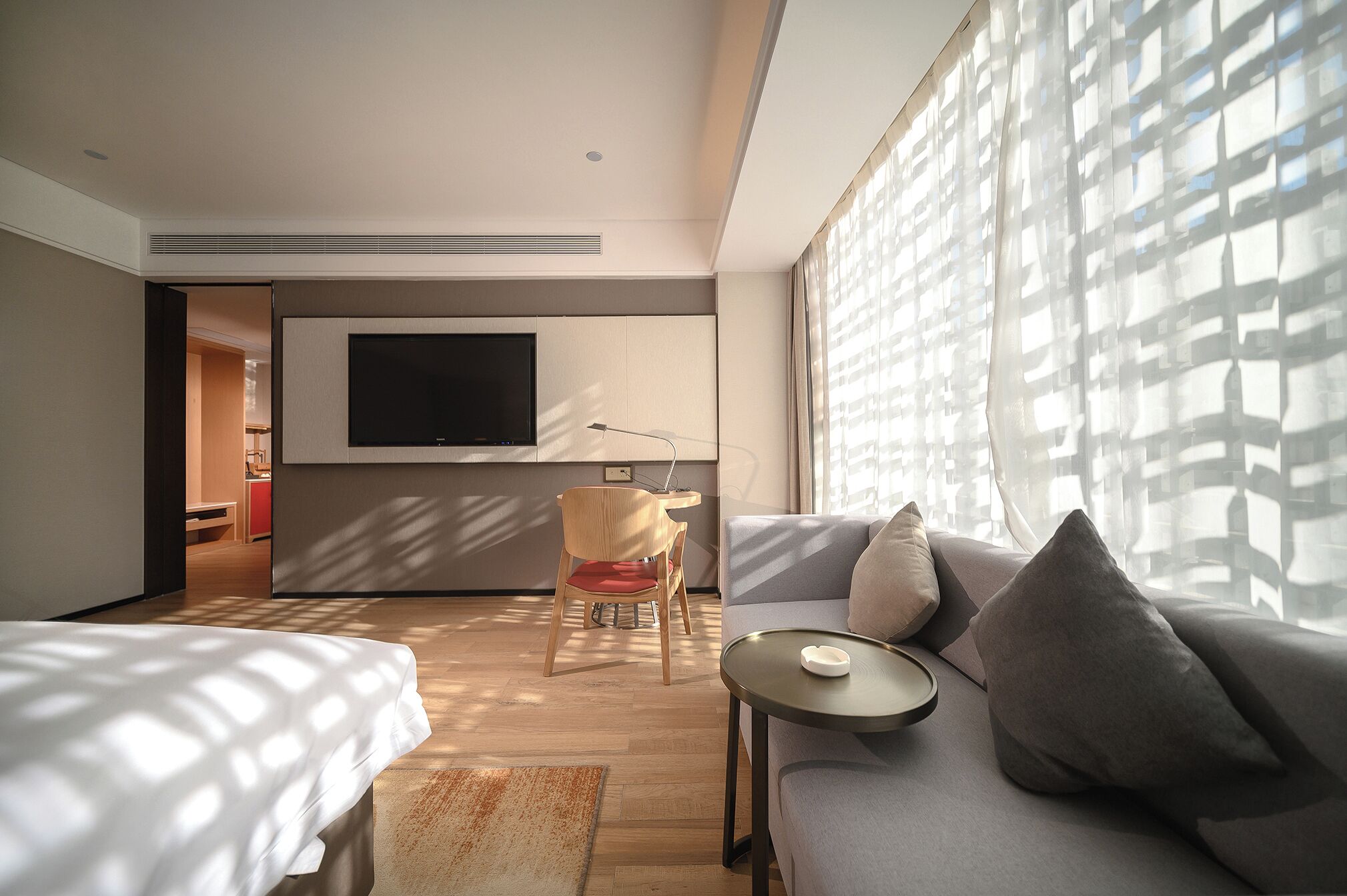 Una habitación de hotel moderna con una cama grande, un sofá, un televisor montado en la pared y una ventana con vistas.