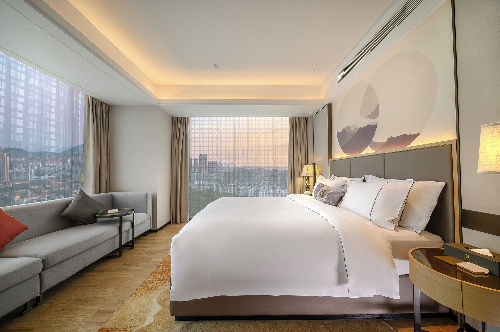 A hotel room with a large bed, a sofa, a desk, and a city view.