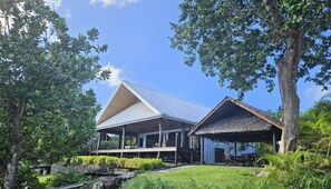 A modern house with a large porch and a covered outdoor seating area, surrounded by lush greenery.