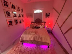A bedroom with a bed, framed pictures on the wall, a window, and a nightstand with a lamp. - The Swift Lake House (Somerset)