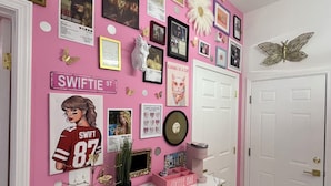 Eine rosa gestaltete Wand mit verschiedenen gerahmten Bildern, einer Kaffeebar und einer weißen Tür.