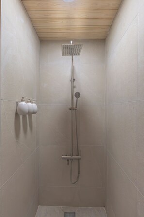 A shower with a wooden ceiling, a handheld showerhead, and two wall-mounted dispensers.