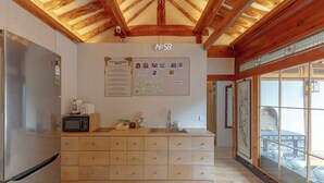 A kitchen with a wooden ceiling, a stainless steel refrigerator, a microwave, a sink, and a bulletin board with various notes. - Damitory inn Dongmyo (Seoul)