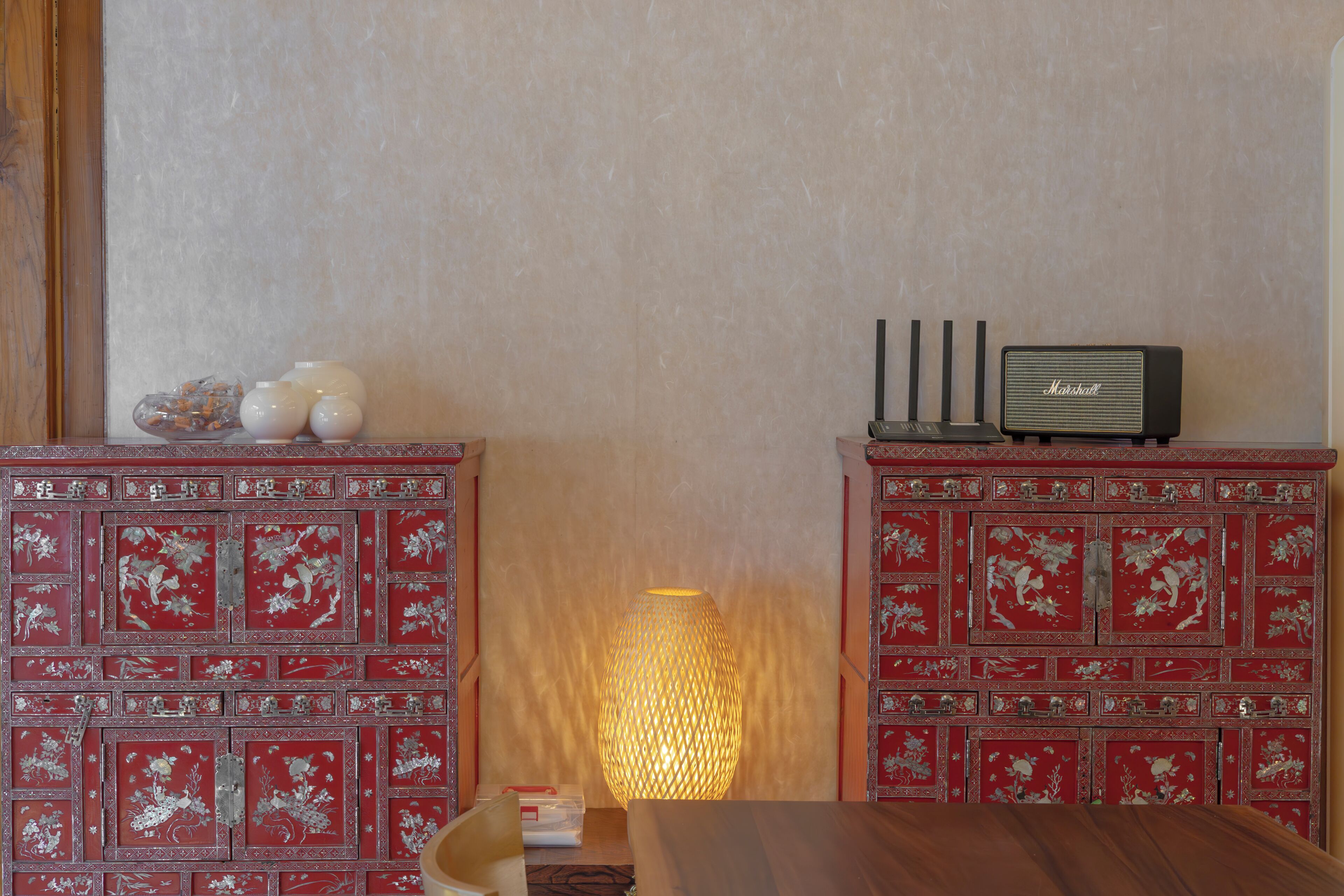 Una habitación con una mesa de madera, un armario rojo con diseños florales, una lámpara y un radio Marshall.