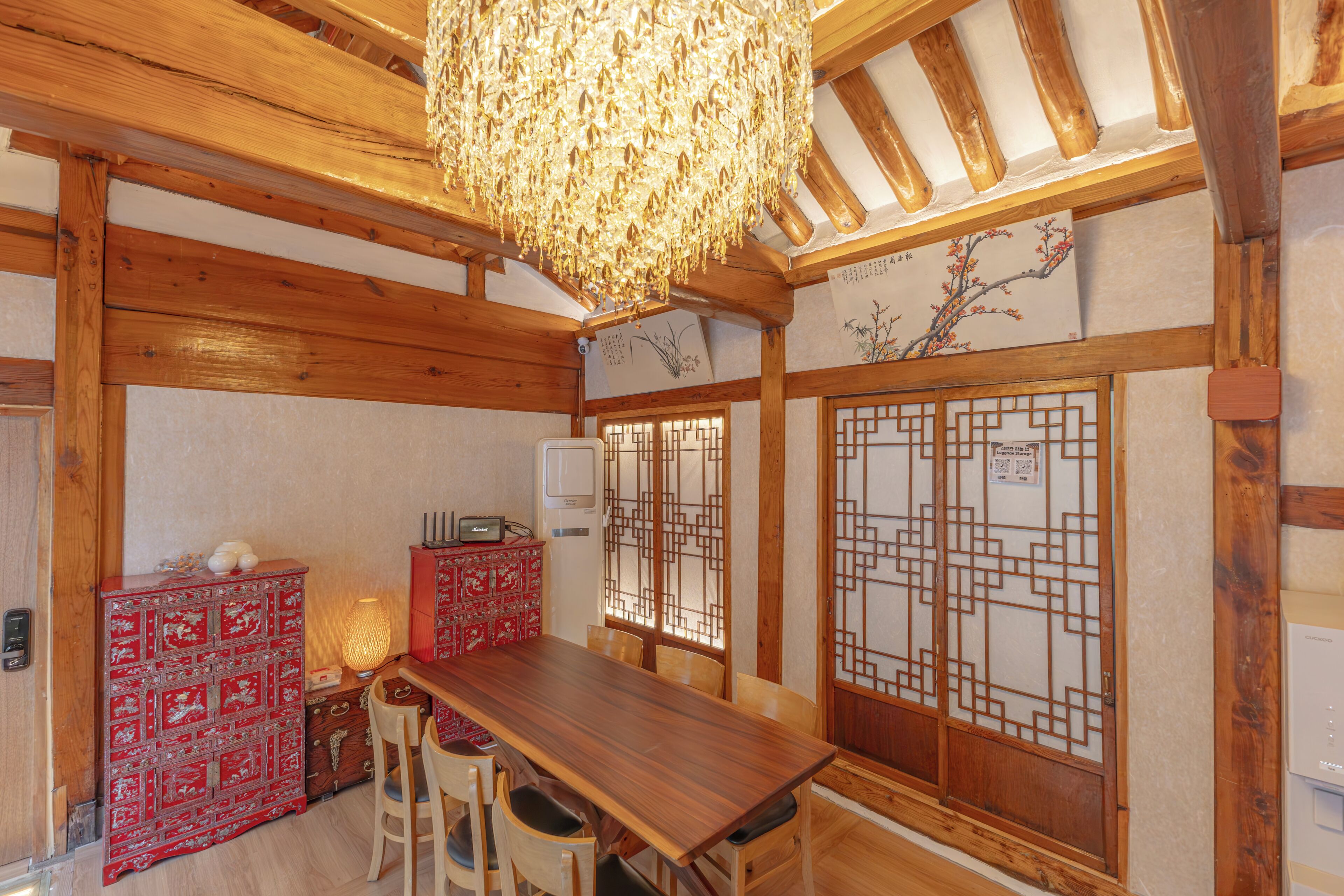 A traditional Japanese room with a wooden table, chairs, a red cabinet, and a decorative screen.