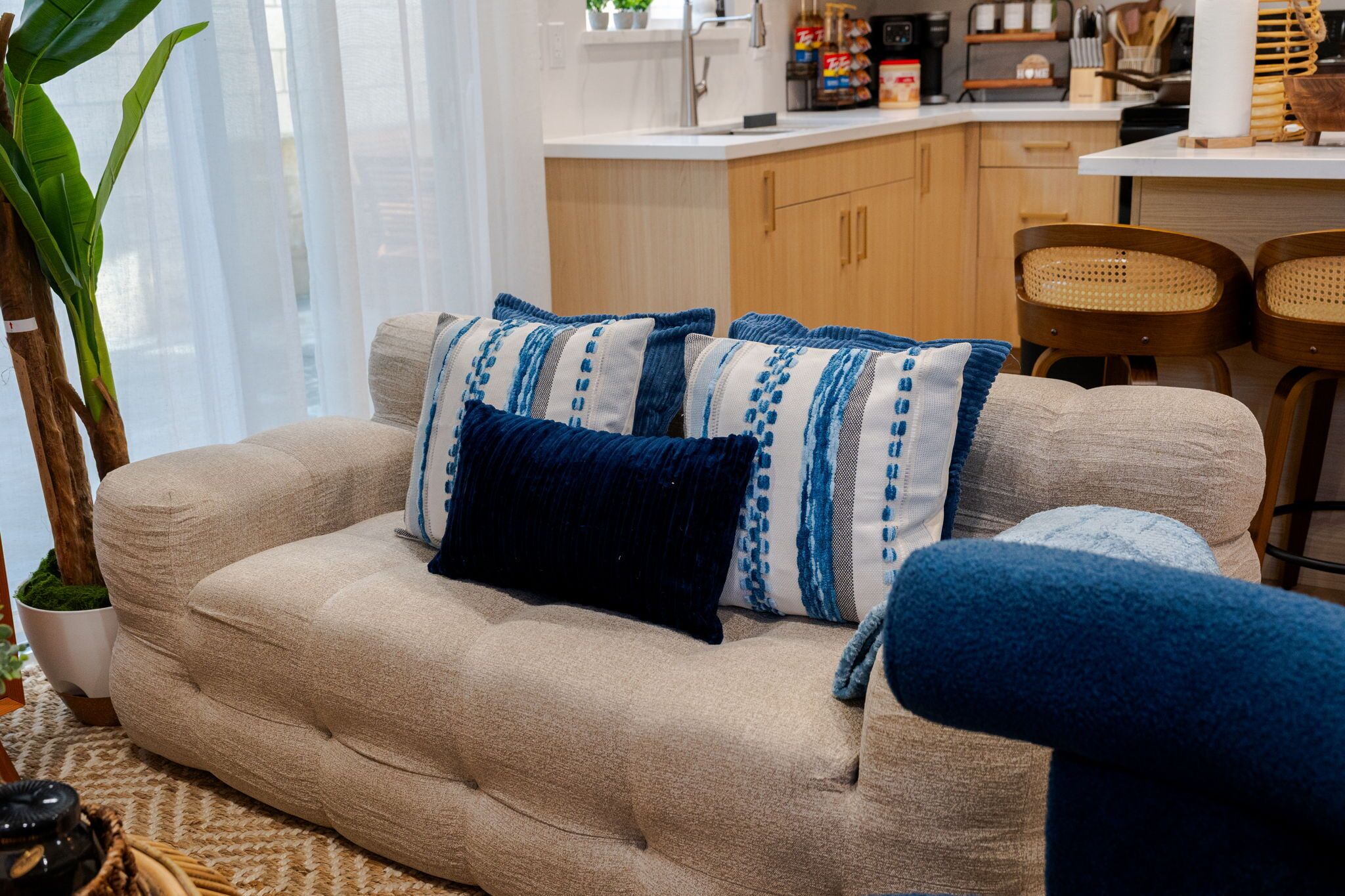 Un sofá color beige con cojines estampados en azul y blanco, una planta en maceta y sillones de mimbre en un salón.