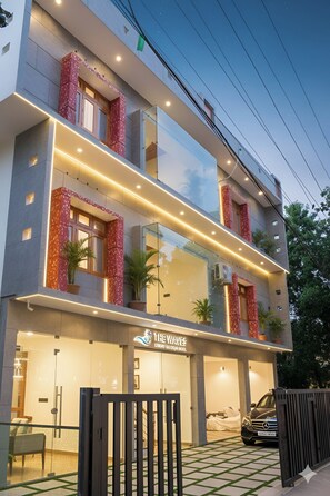 A modern hotel with a glass facade, red accents on the balconies, and a Mercedes-Benz parked in front. - De Waves (Varkala)