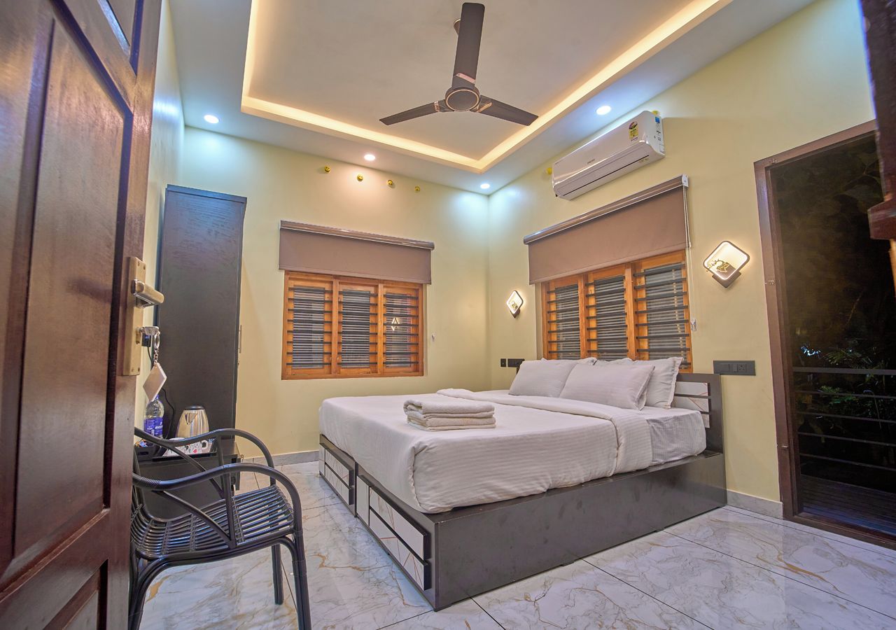 A bedroom with a bed, a desk, and a chair. There is a ceiling fan and an air conditioning unit.