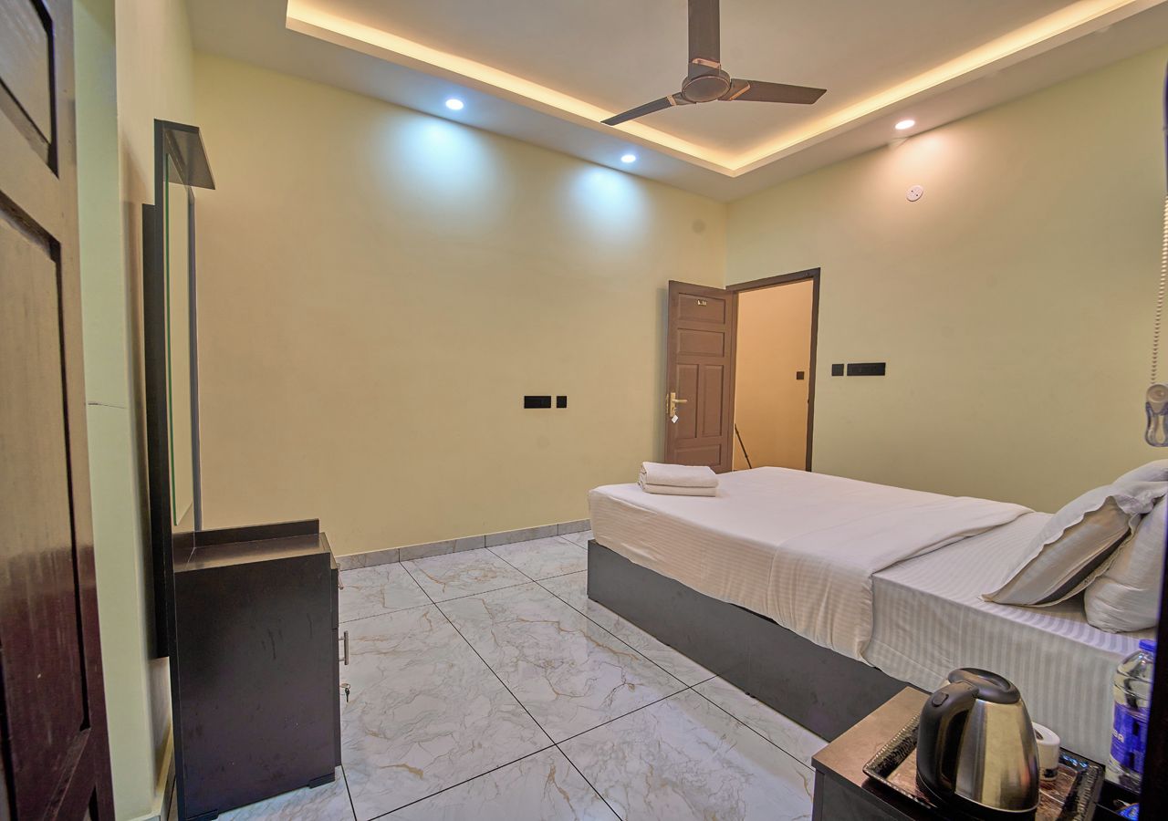 Una habitación de hotel con una cama, un ventilador de techo, una mesita con una tetera y una puerta.