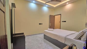 Una habitación de hotel con una cama, un ventilador de techo, una mesita con una tetera y una puerta.