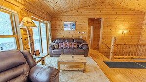 A wooden cabin interior with a leather sofa, a coffee table, and a lamp with a deer design. - Lost on Purpose : Summer Memories Made Here | Cabin for 12 (Wetmore)
