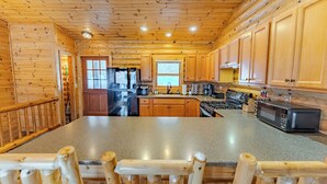 A wooden cabin kitchen with a central island, wooden cabinets, a refrigerator, stove, and a microwave. - Lost on Purpose : Summer Memories Made Here | Cabin for 12 (Wetmore)