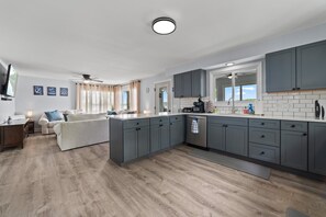Eine moderne Küche mit grauen Schränken, einer integrierten Kochinsel und einem Essbereich mit Sofa und Couchtisch.
