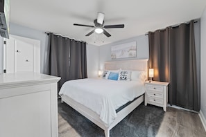Ein Schlafzimmer mit einem Bett, Nachttischen, einem Deckenventilator, einem weißen Kleiderschrank und einem Gemälde an der Wand.