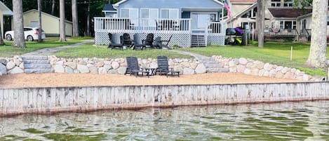 Una cabaña junto al lago con muelle, asientos al aire libre y un muro de piedra.