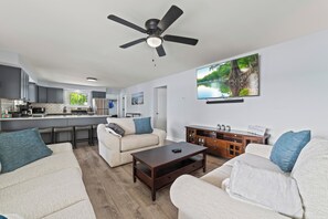 A modern living room with a sofa, coffee table, and a TV mounted on the wall. - Serenity All Year Long : Lakefront 3BR, 3BA retreat with hot tub, dock, kayaks & fire pit. (Cheboygan)