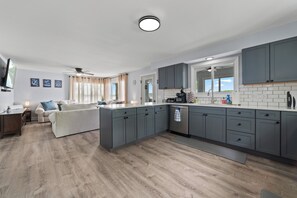 Une cuisine moderne avec des meubles gris, un îlot central et un coin repas comprenant un canapé et une table basse.