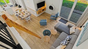 A modern living room with a sofa, coffee table, and TV. There is a dining area with a table and chairs. The room has a large sliding glass door leading to a garden. - Seelykke 304 by Interhome (Lembruch)
