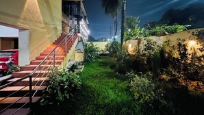 A nighttime view of a building with a staircase leading to a covered area, surrounded by greenery and a parked car. - Venus Heritage (Bhubaneshwar)