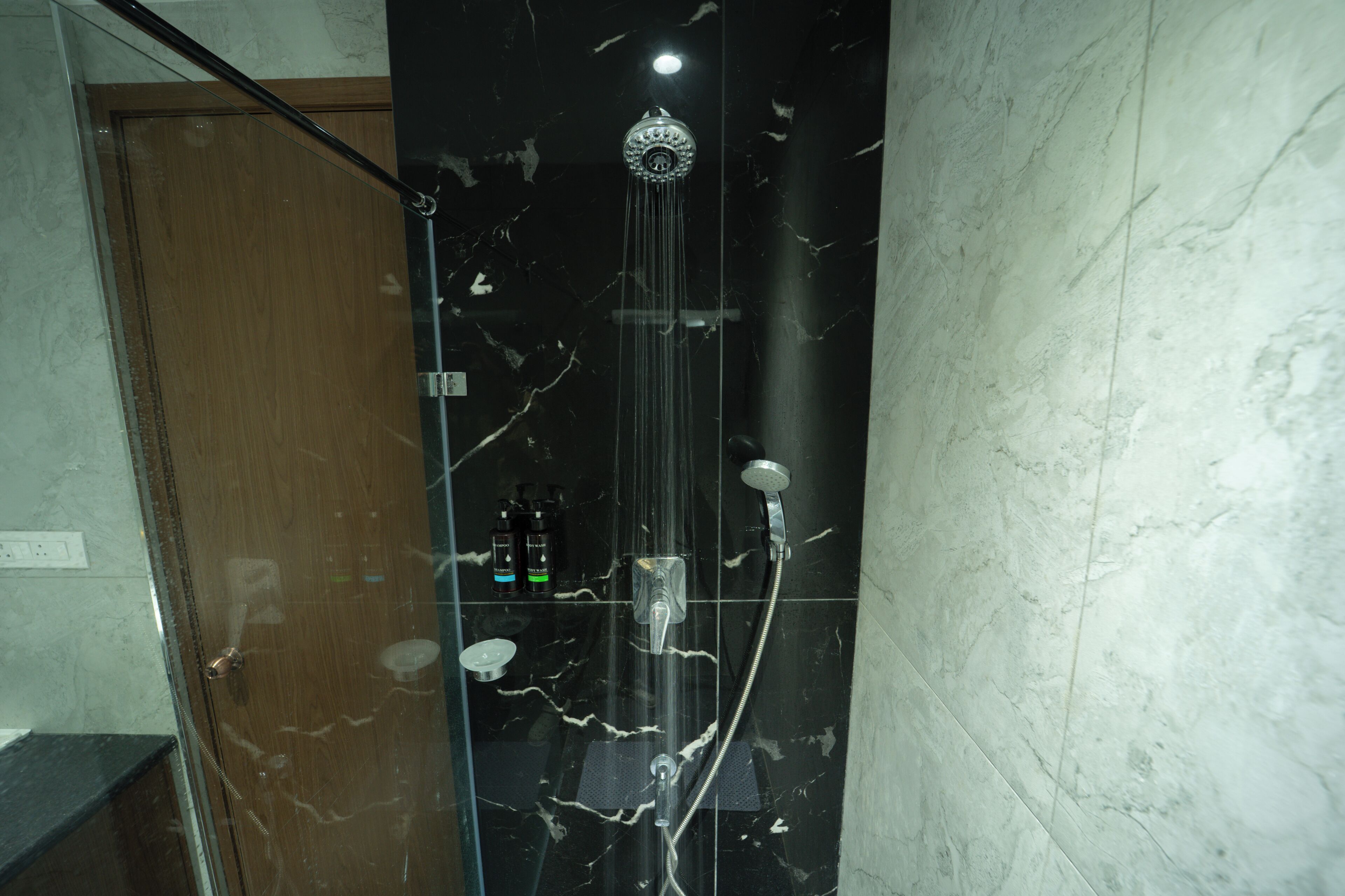 Een douche met een handdouche en een wandmengkraan, voor een marmeren wand.