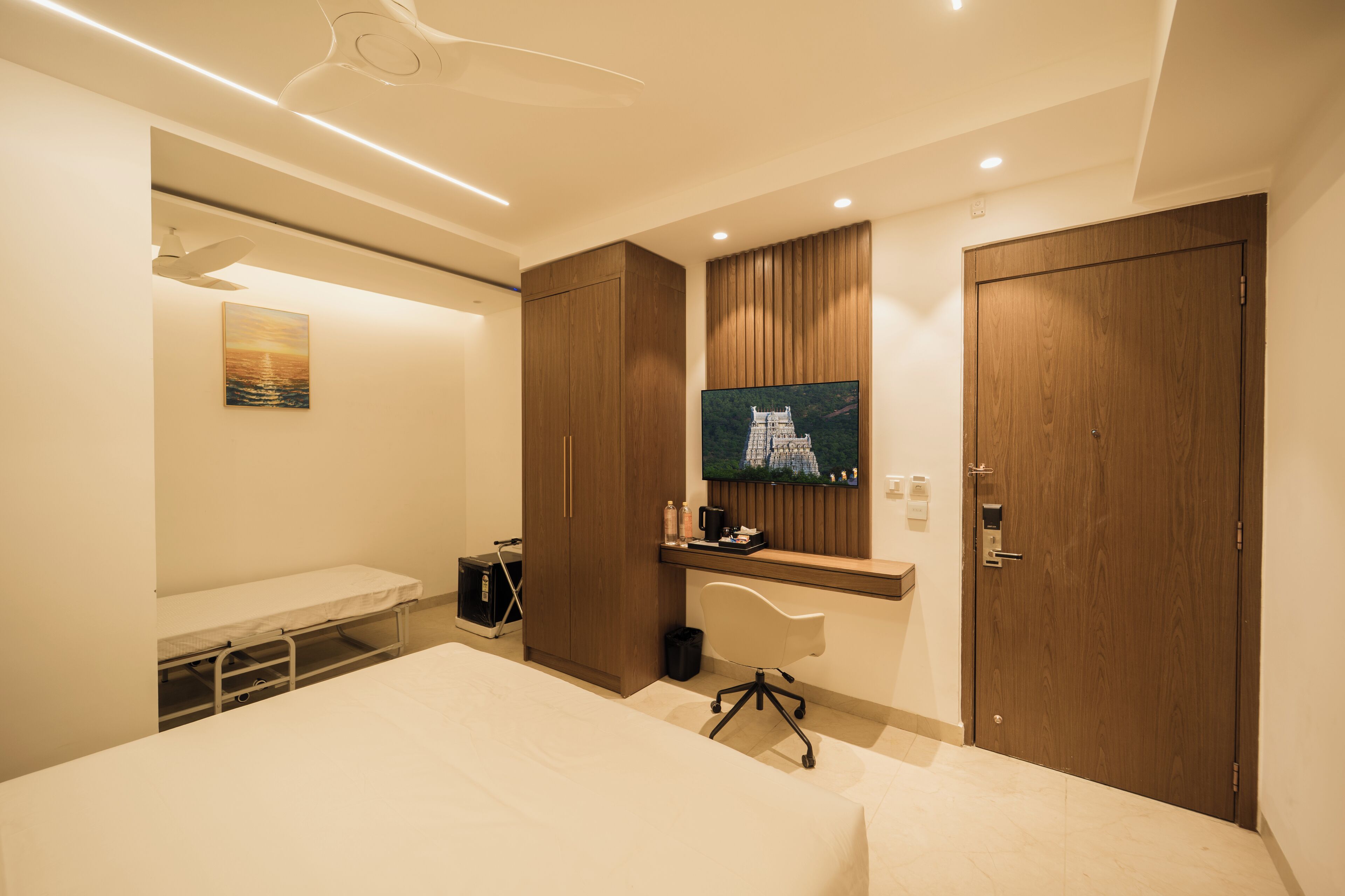 Een moderne hotelkamer met een bed, een bureau, een stoel, een aan de muur bevestigde televisie en een houten garderobe.