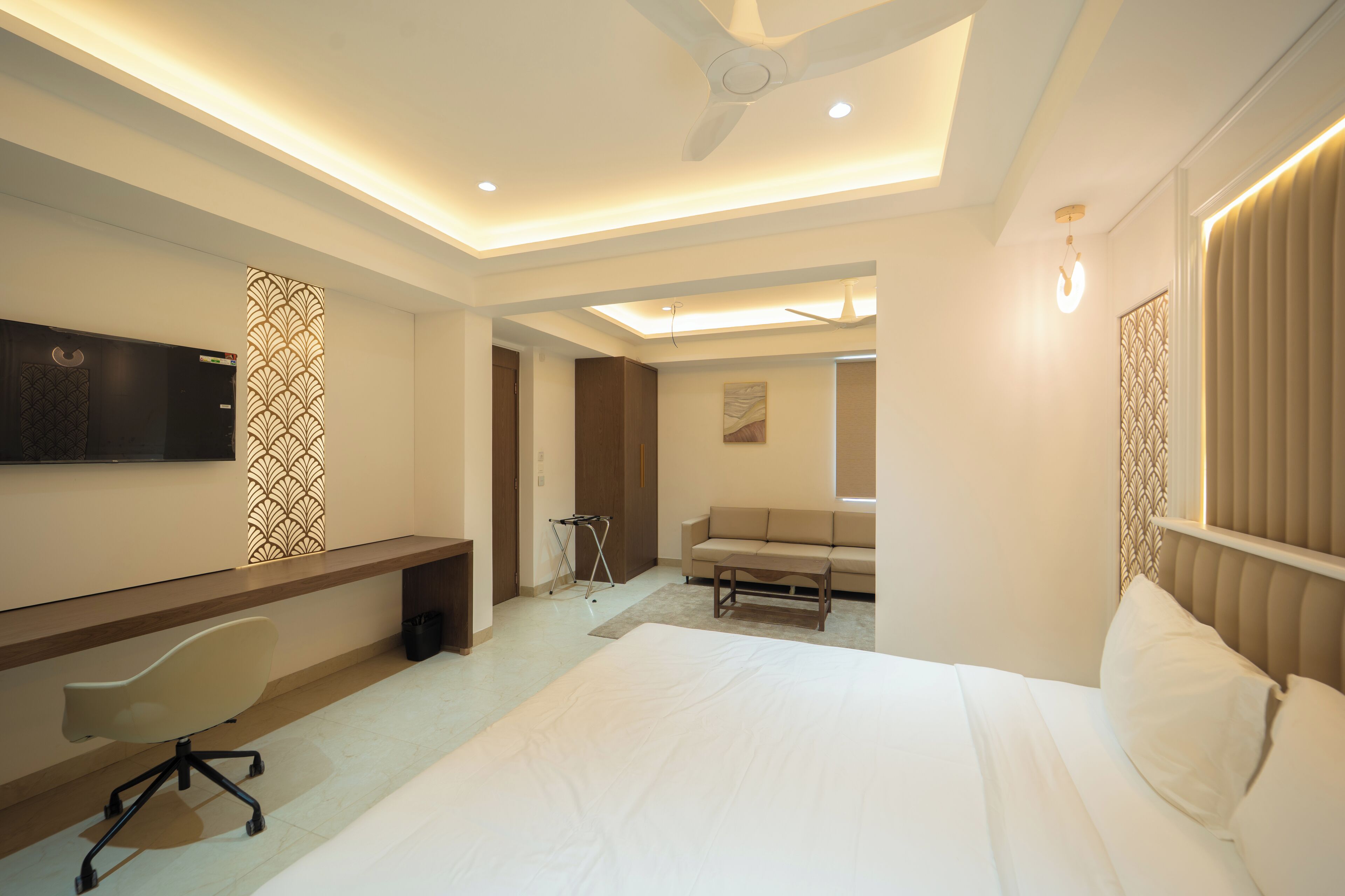 A hotel room with a bed, a desk, a chair, a TV, and a ceiling fan.
