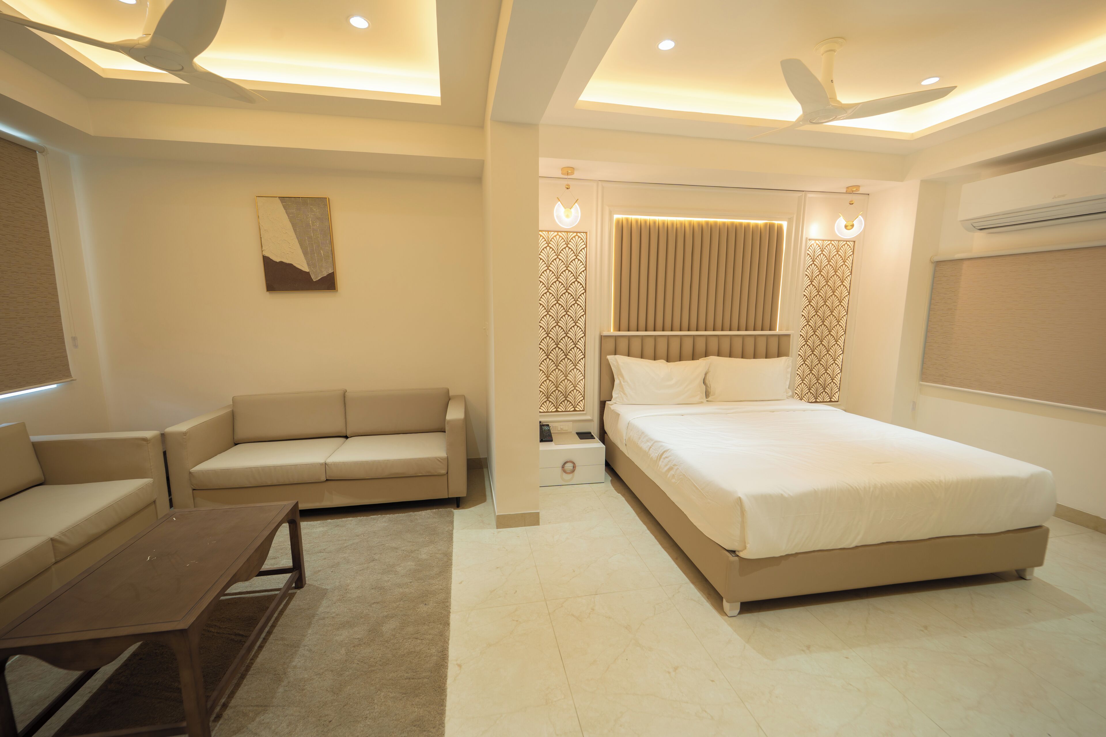 A modern hotel room with a bed, a sofa, a coffee table, and a ceiling fan.