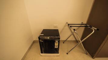 Una habitación con un electrodoméstico negro, posiblemente una lavadora y secadora, y una silla plegable de metal apoyada en la pared.