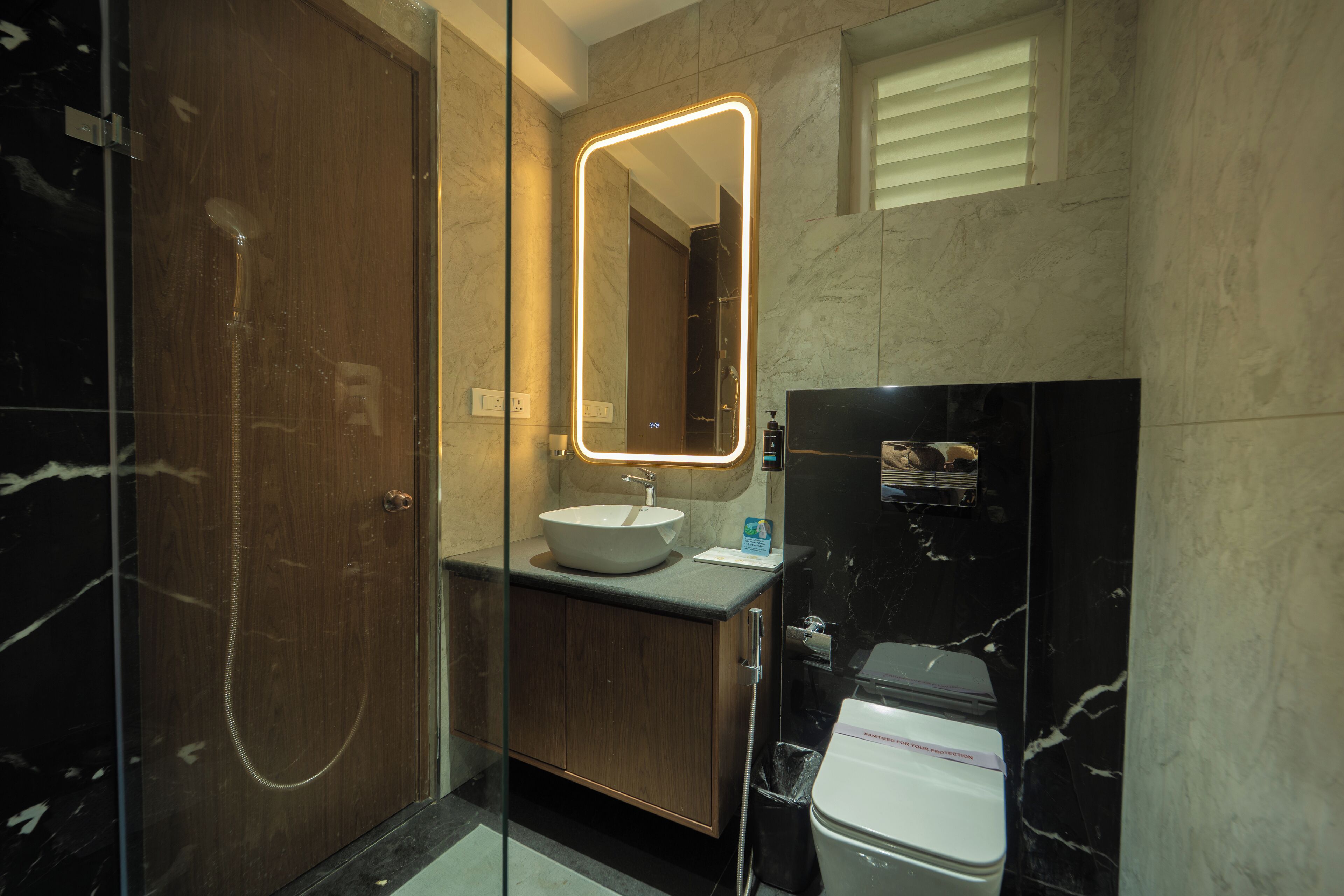 A modern bathroom with a glass-enclosed shower, a wooden vanity, a white sink, and a black marble wall.