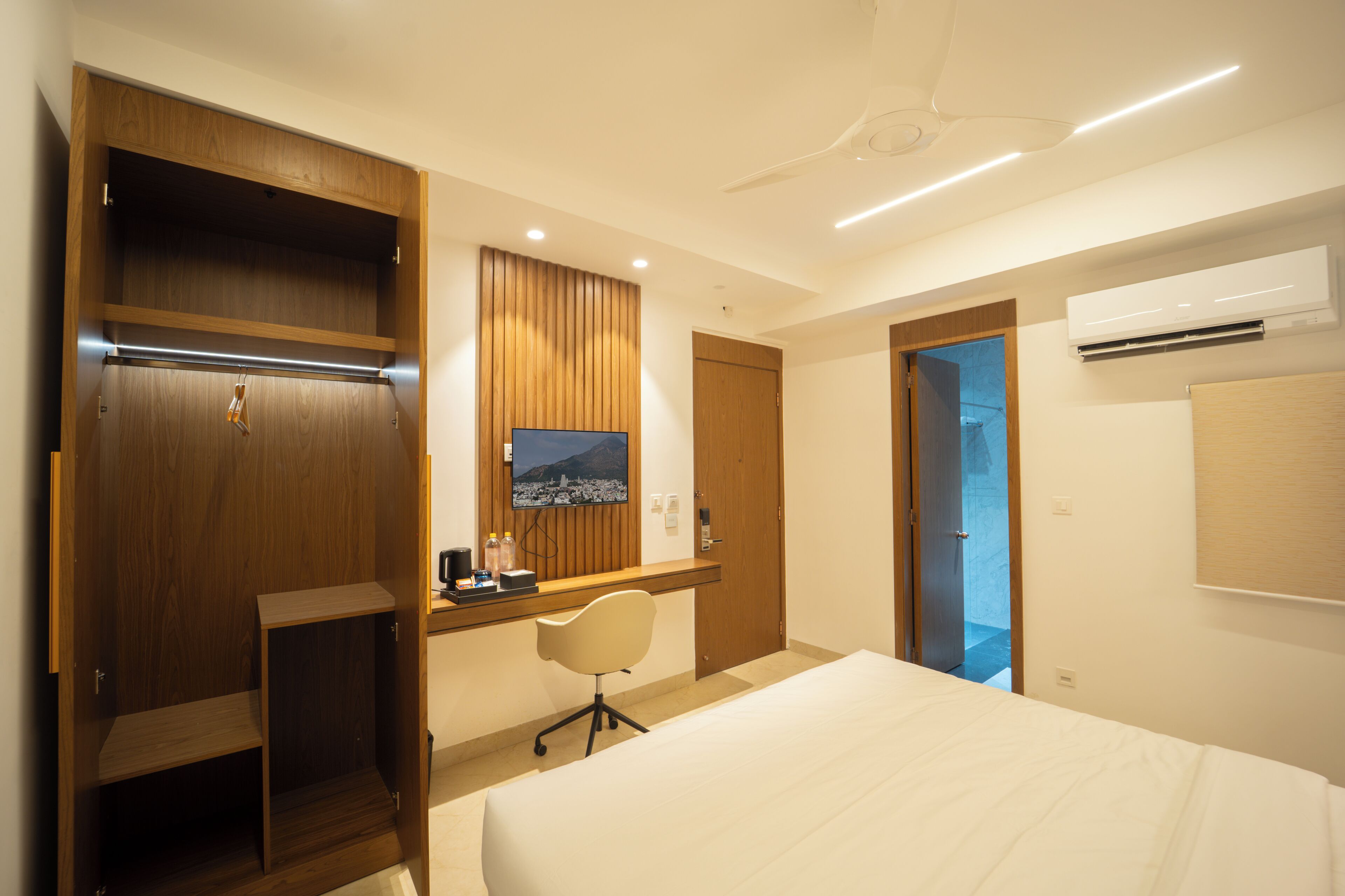 A hotel room with a bed, a desk with a chair, a television, and a wardrobe.