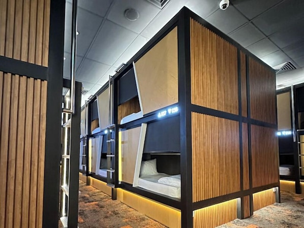 A row of bunk beds with wooden paneling and built-in lighting, in a modern hotel room. - Napzone KLIA T2 (Sepang)