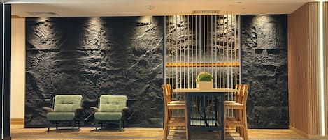 A modern interior with a stone wall, two green armchairs, a wooden dining table with chairs, and a potted plant.