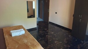 Habitación de hotel con mesa de masajes, suelo de mármol oscuro, armario y espejo.