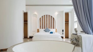 Quarto de hotel moderno com uma banheira grande e redonda, uma cama bem arrumada com cabeceira de madeira e vista da cidade através de amplas janelas.