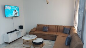 Ein modernes Wohnzimmer mit einem braunen Sofa, zwei runden Couchtischen, einer weißen TV-Konsole und einem gemusterten Teppich.