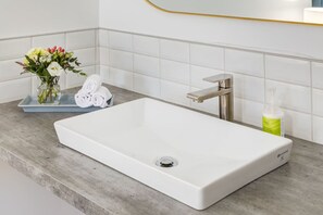 A bathroom with a white sink, a towel rack, and a small vase with flowers. - Gateway Suites: Cozy Getaway Near Banff/Canmore (Harvie Heights)