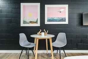 A modern room with a black brick wall, two framed artworks depicting landscapes, a round wooden table with two grey chairs, and a small wooden sculpture on the table. - Gateway Suites: Cozy Getaway Near Banff/Canmore (Harvie Heights)