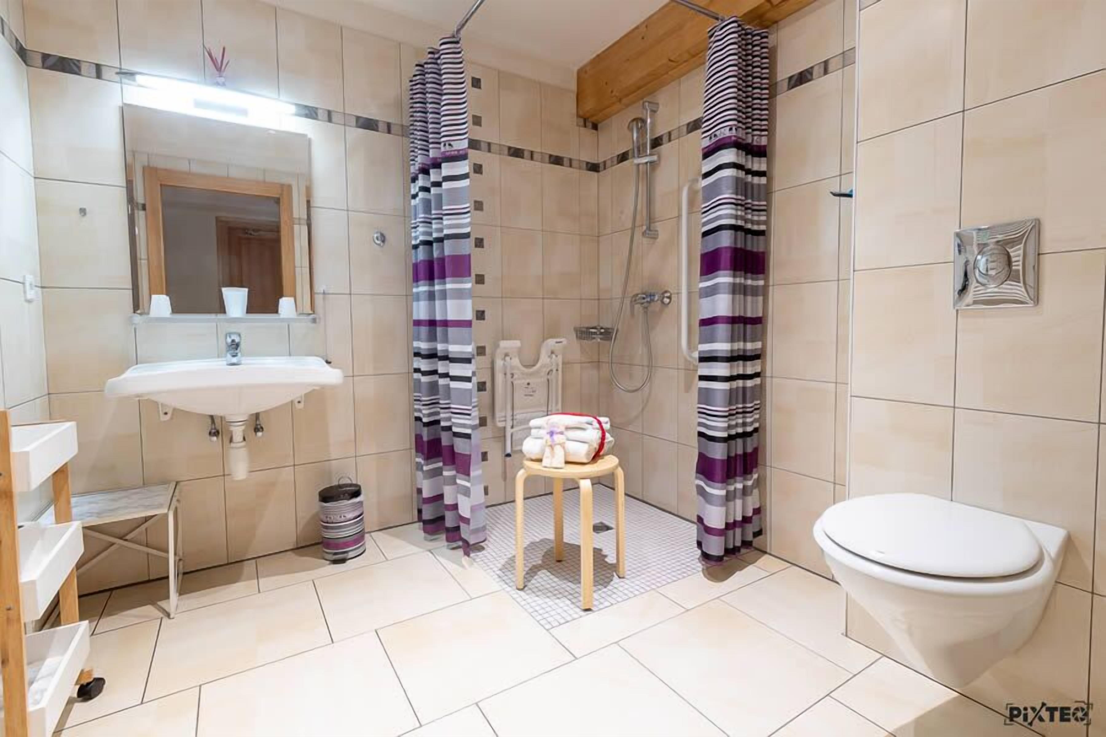 A bathroom with a sink, toilet, shower, and a small stool with towels.