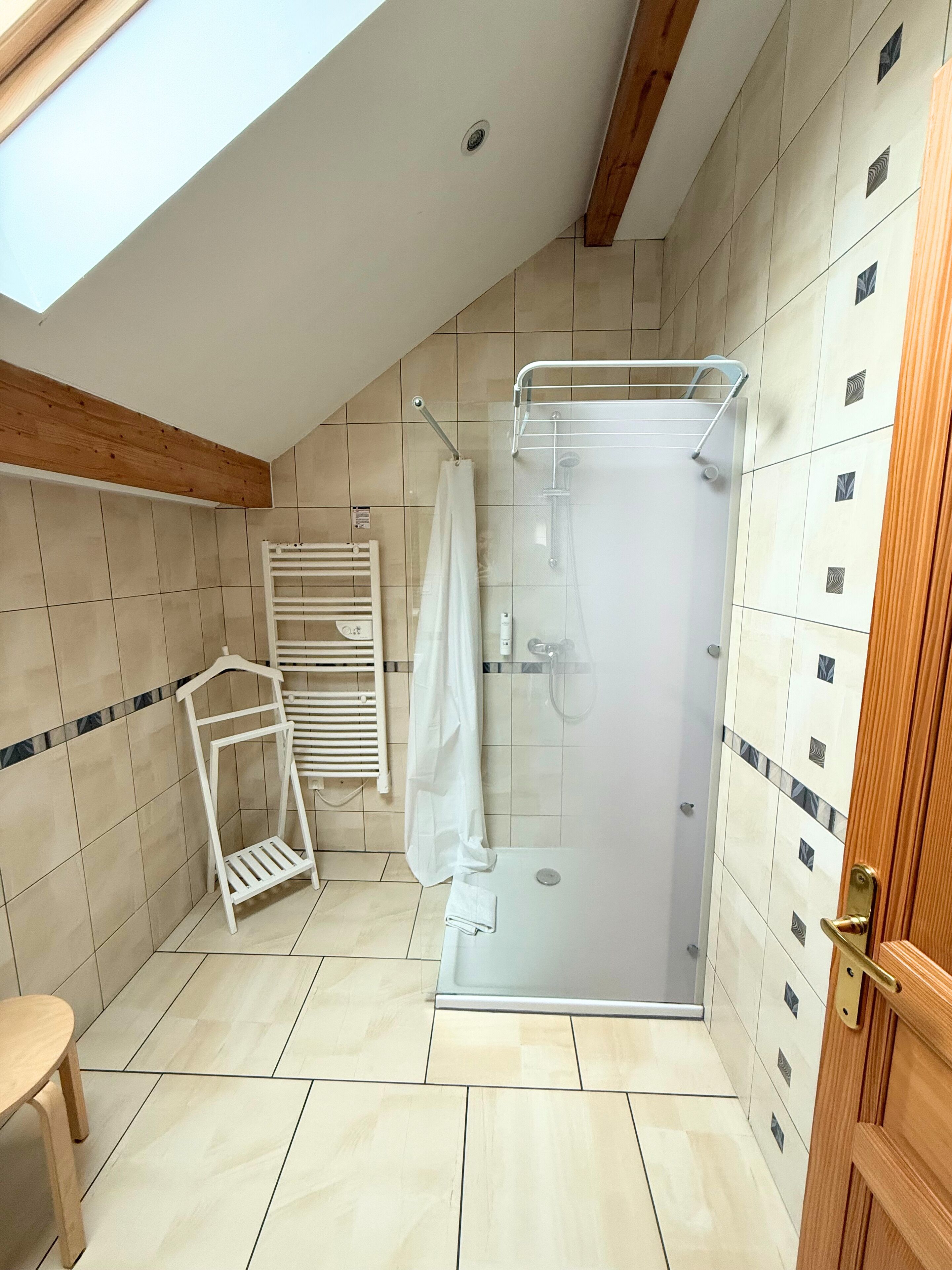 Un baño moderno con cabina de ducha de vidrio, un perchero blanco y techo de madera.