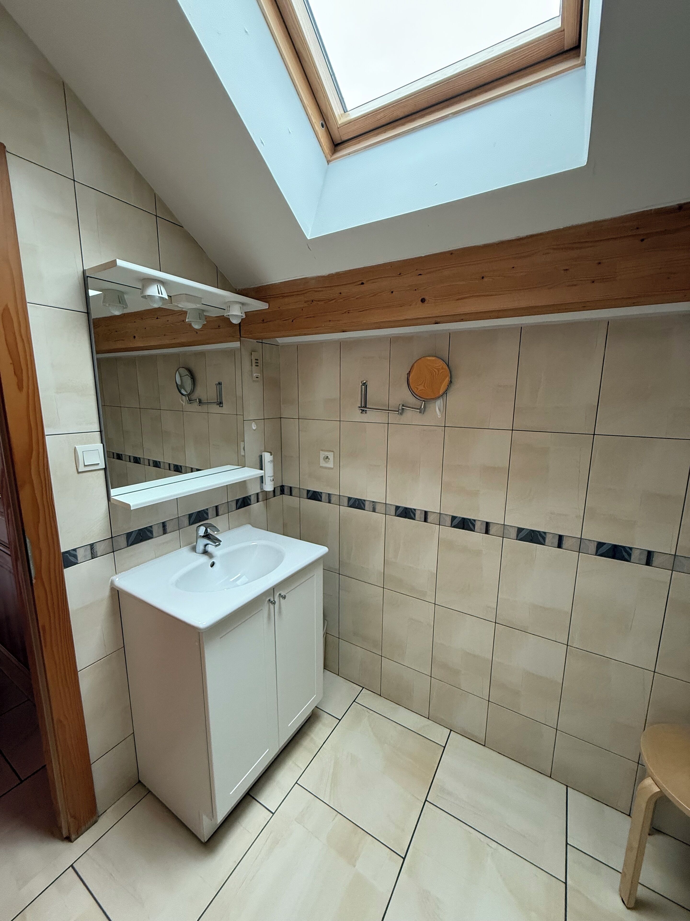 A modern bathroom with a skylight, a sink with a mirror, and a wooden beam ceiling.